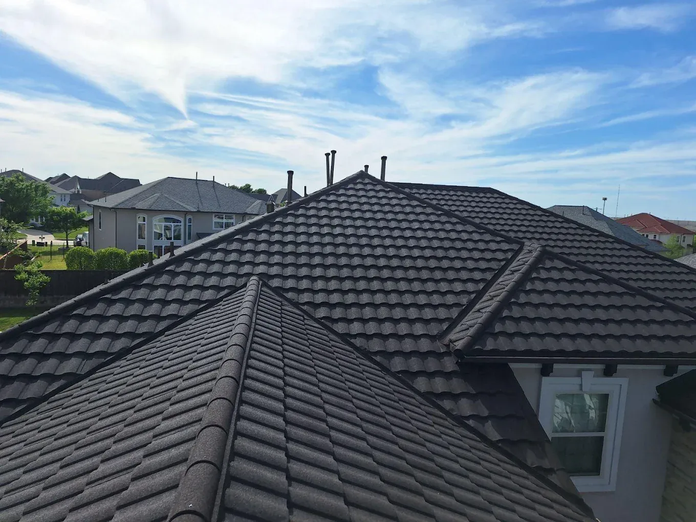Charcoal stone-coated steel tile roof with hip and ridge caps on a two-story Dallas–Fort Worth home